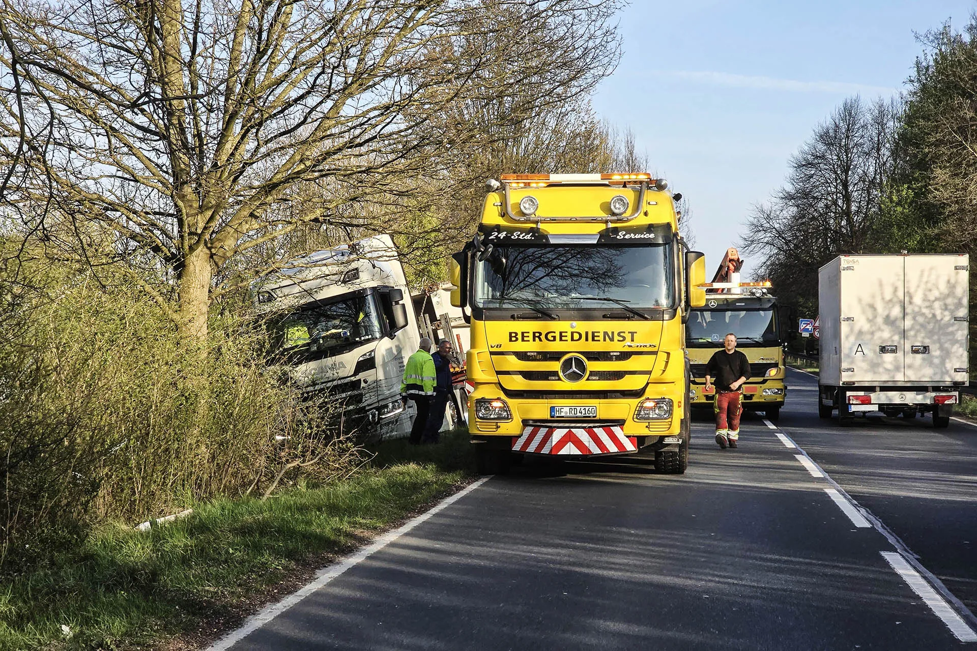 Zwei gelbe Bergedienst-LKW von R.D. Spezial-Transporte sichern einen im Graben gelandeten weißen Sattelzug auf einer Landstraße ab.