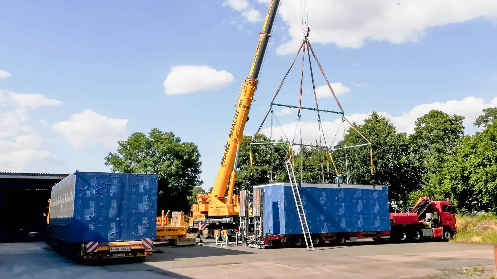 Ein Baucontainer der mit einem Kran auf einen Spezialtransporter gehieft wird.