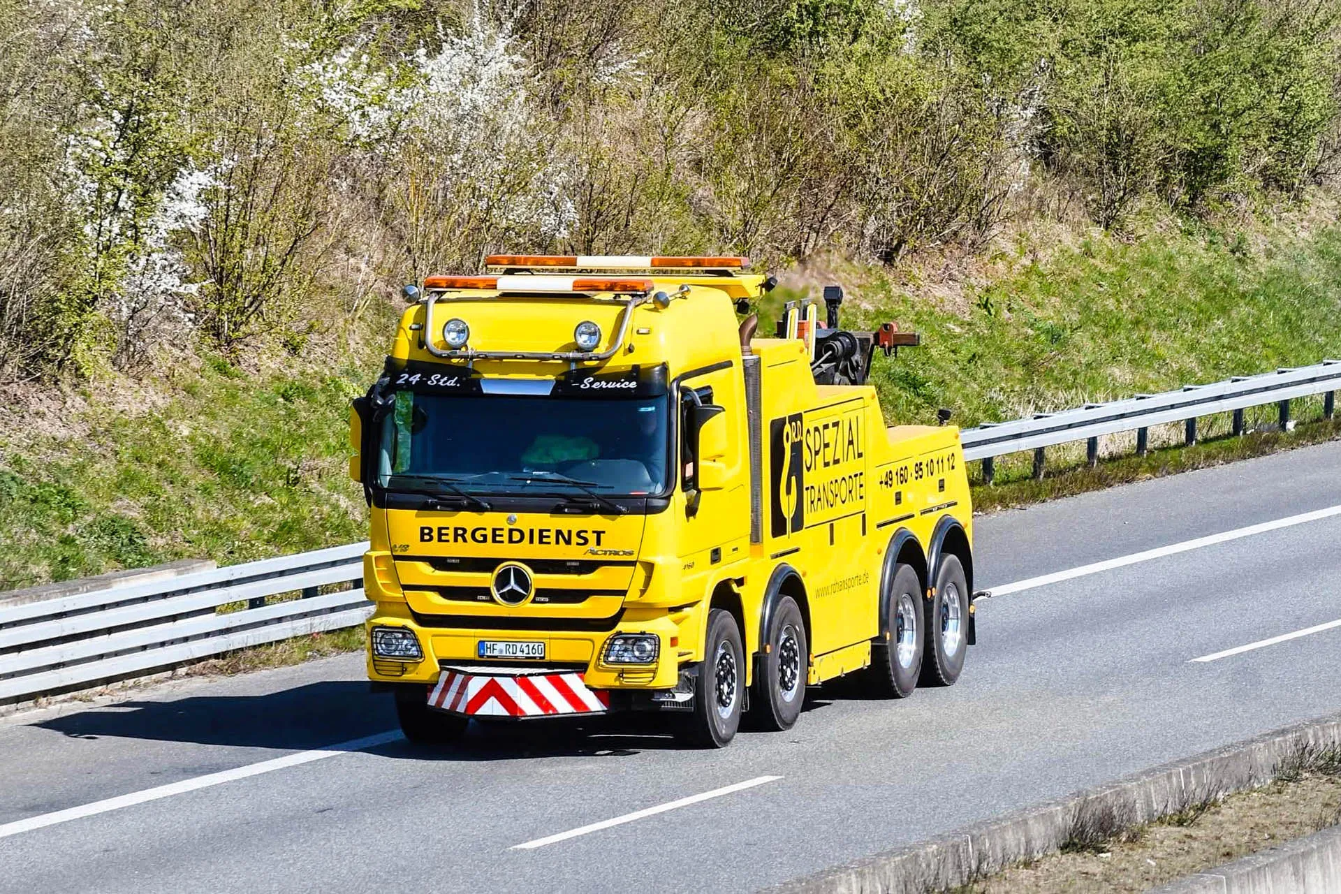 Gelber Mercedes-Benz Actros Bergedienst-LKW von R.D. Spezial-Transporte mit Warnleuchten fährt auf einer Autobahn mit Leitplanke und grüner Böschung.