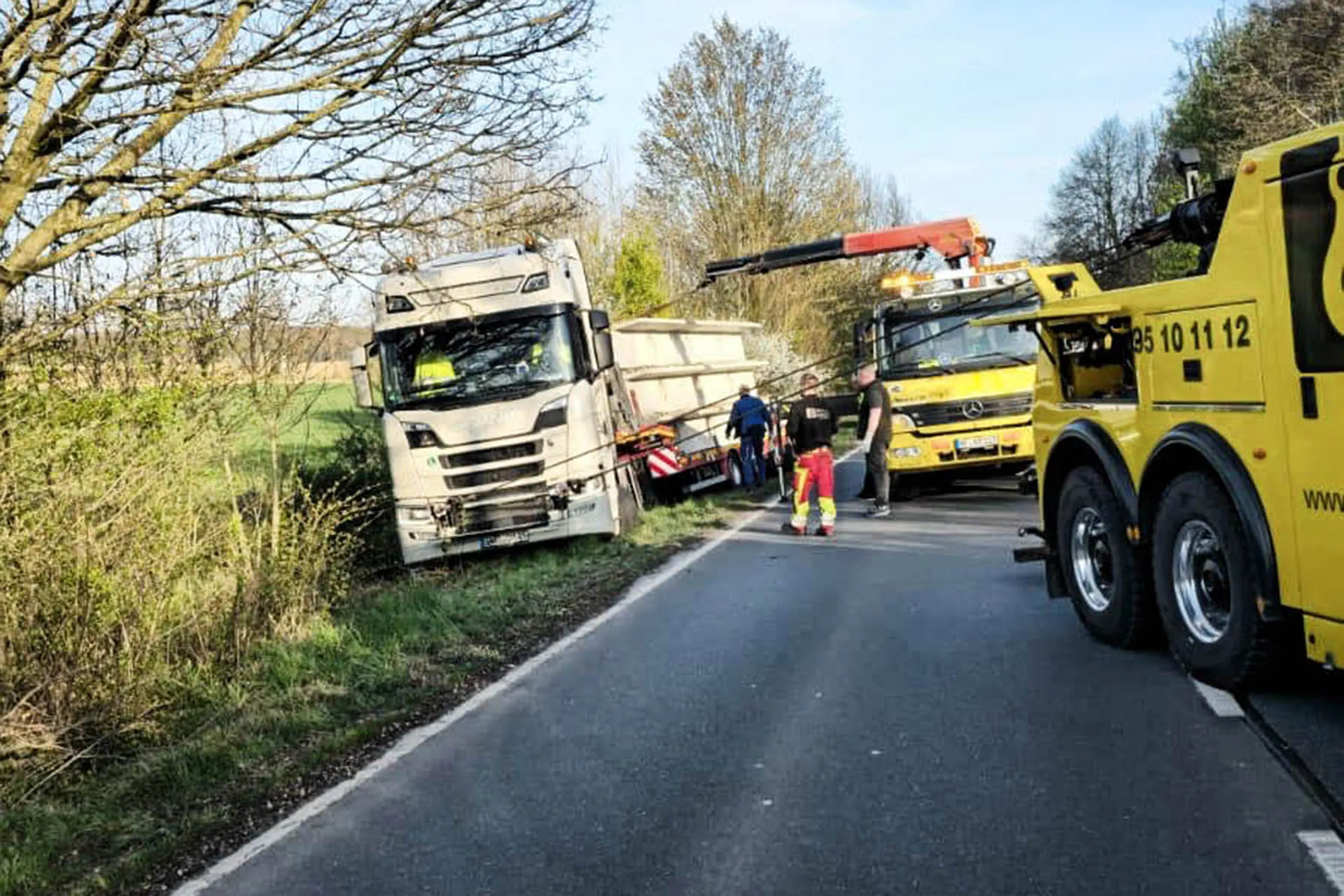 Bergung eines weißen Scania Sattelzugs mit Container, der am Straßenrand im Graben feststeckt, durch zwei gelbe Abschleppfahrzeuge von R.D. Spezial-Transporte.