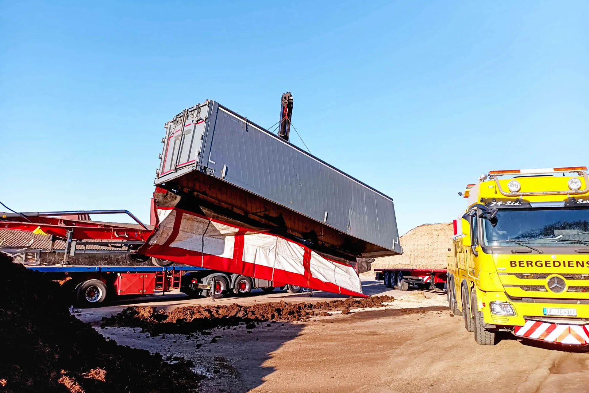 Ein Ladekran hebt einen großen, beschädigten Container-Auflieger an, während ein gelber Bergedienst-LKW von R.D. Spezial-Transporte bereitsteht.