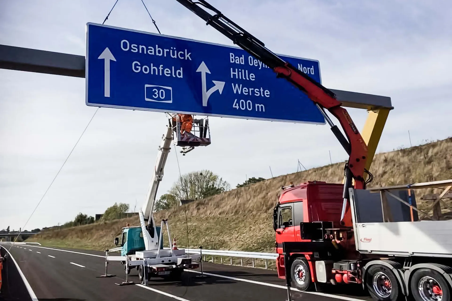 Montage eines großen Autobahnschilds (Ausfahrt Osnabrück/Gohfeld) durch einen LKW mit ausgefahrenem Ladekran und Arbeitsbühne.
